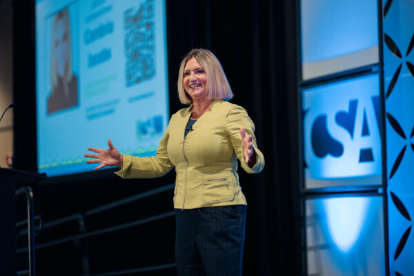 Cambria Jacobs presenting on stage in a yellow jacket at a CSA event